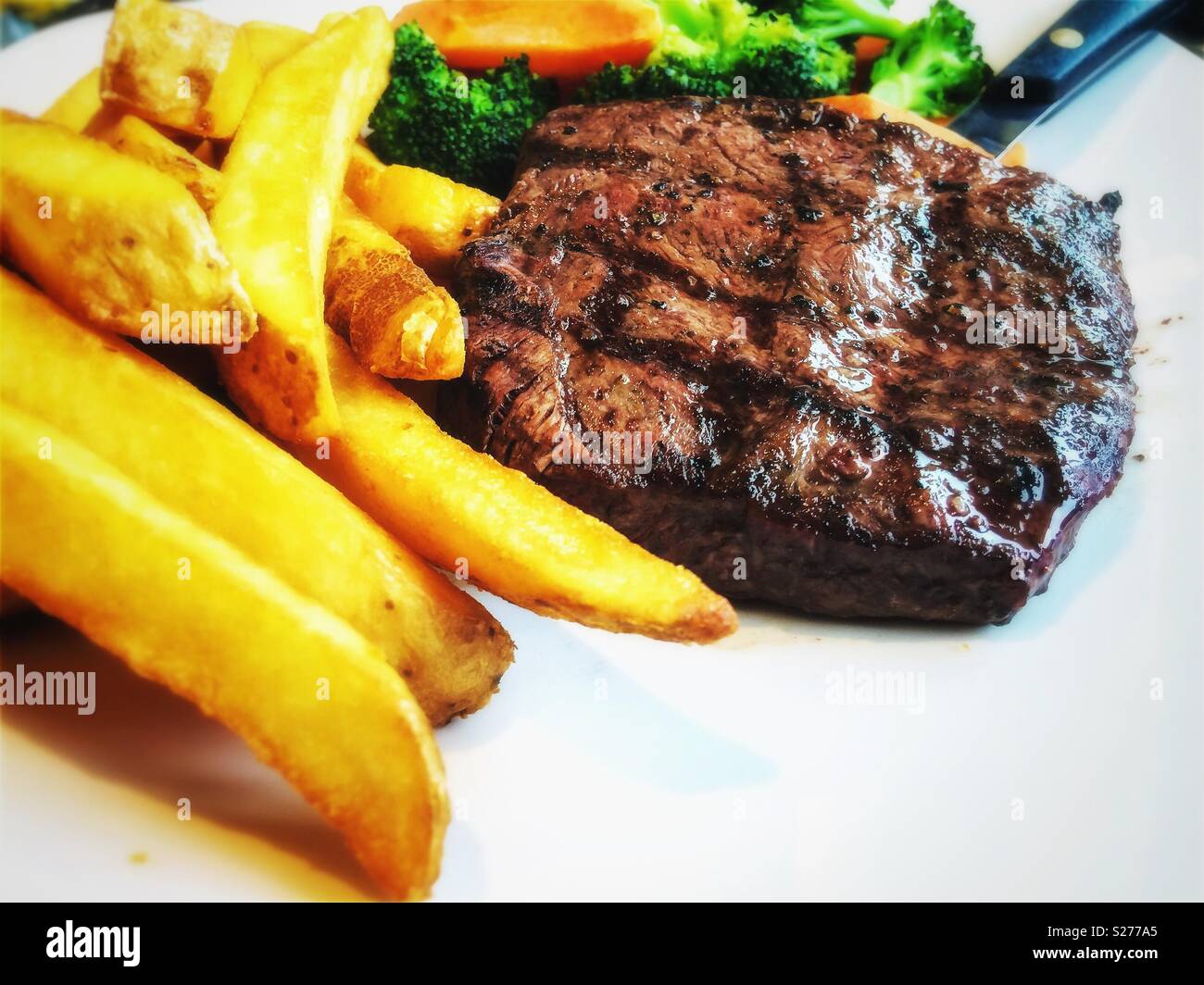 Bügeleisen Steak mit Pommes frites und Gemüse auf dem Teller. - Smartphone-aufgenommenes Stockfoto