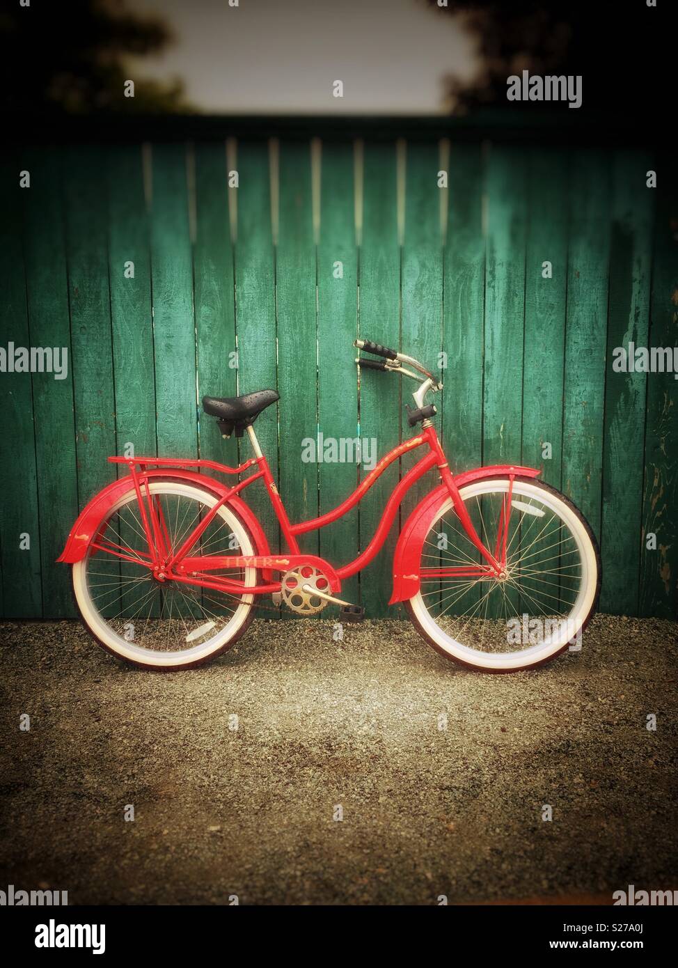 Vintage red Flyer Fahrrad mit weißen Reifen lehnte sich gegen eine grüne Holzzaun auf einem Schotterweg. Stockfoto