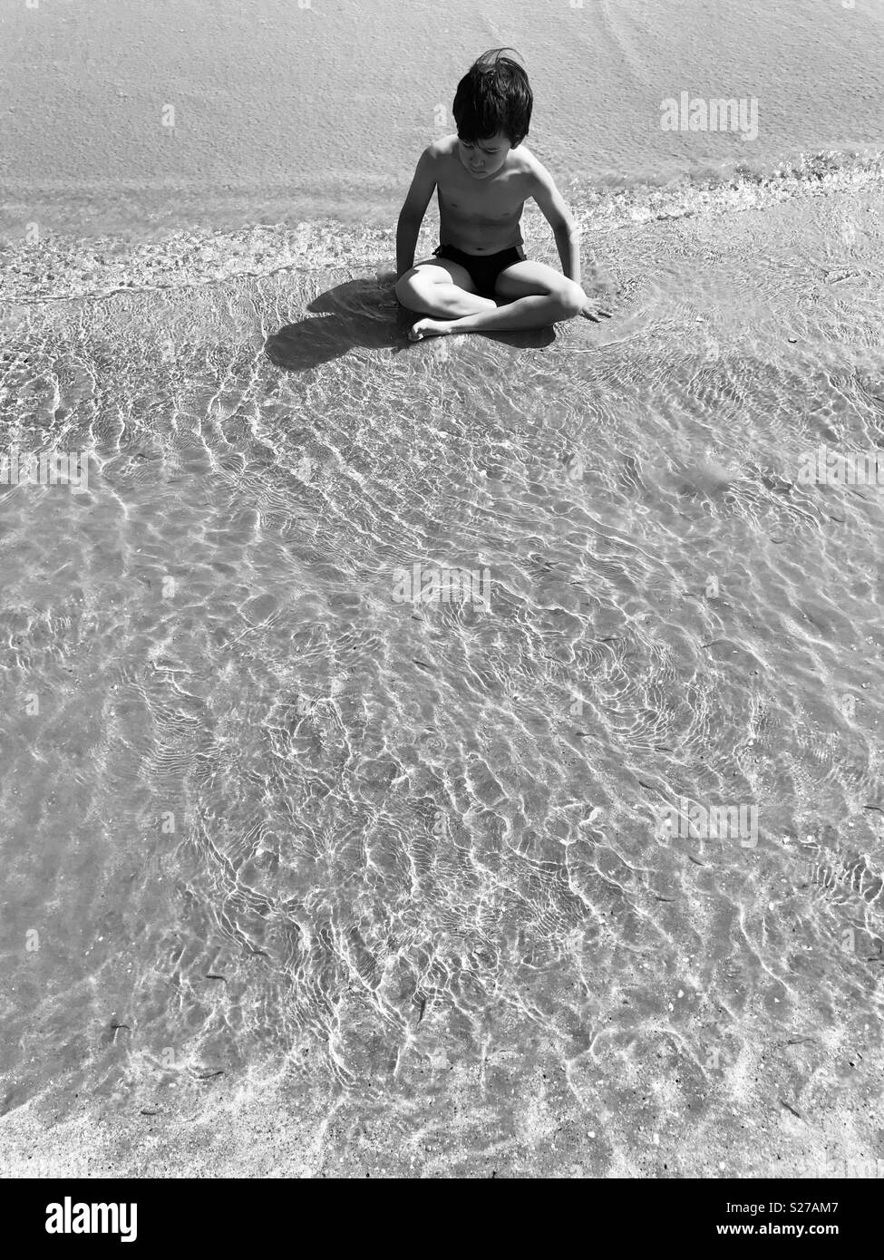 Kind sitzen gekreuzten Beinen im seichten Wasser. Schwarz-weiß Foto. Stockfoto