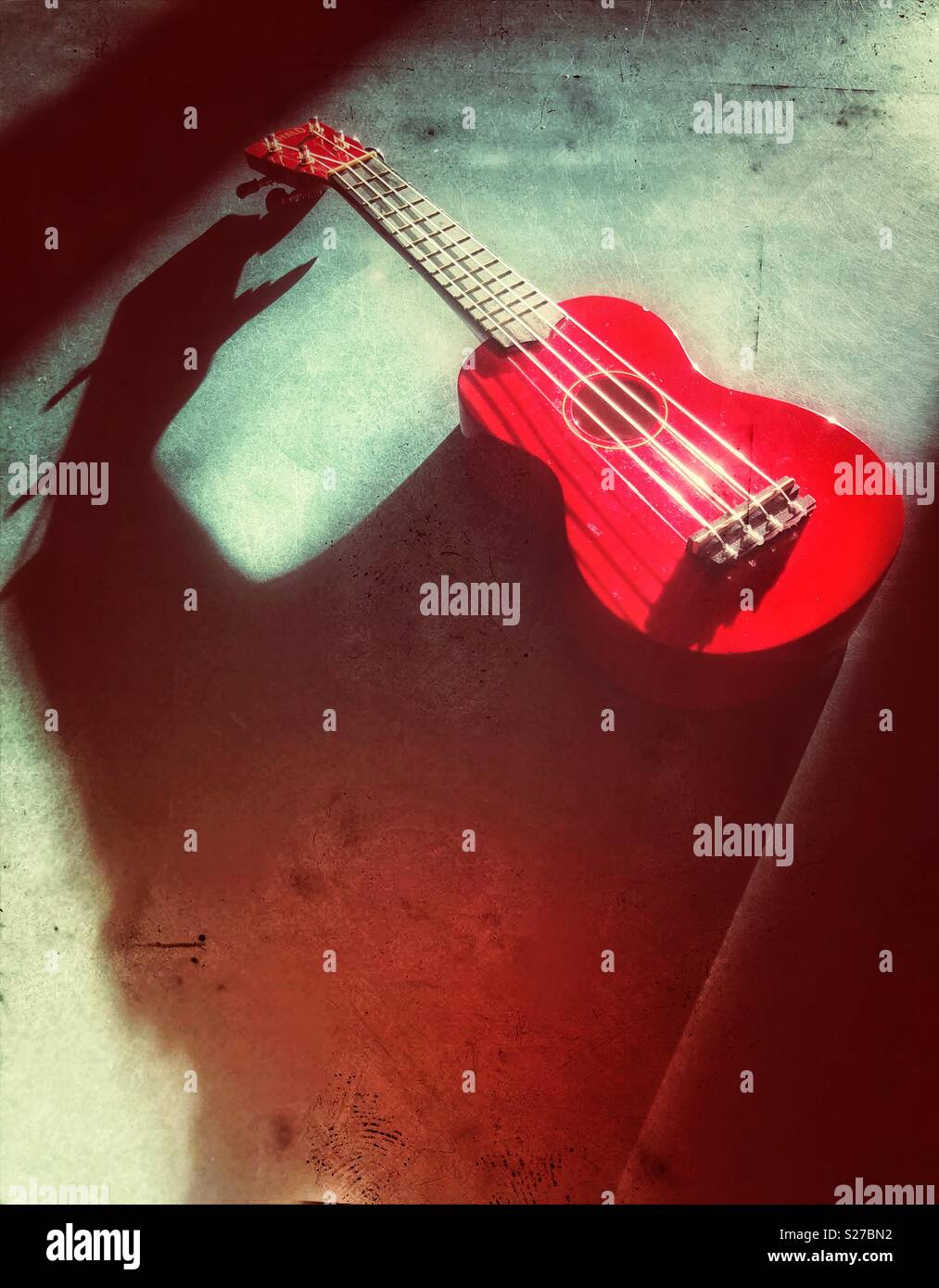 Red ukulele auf rustikale Oberfläche in der Sonne mit dramatischen langen Schatten Stockfoto