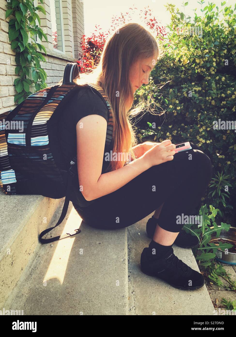 Tween Schulmädchen mit langen blonden Haaren sitzen auf Schritt tragen Rucksack am Smartphone suchen Stockfoto