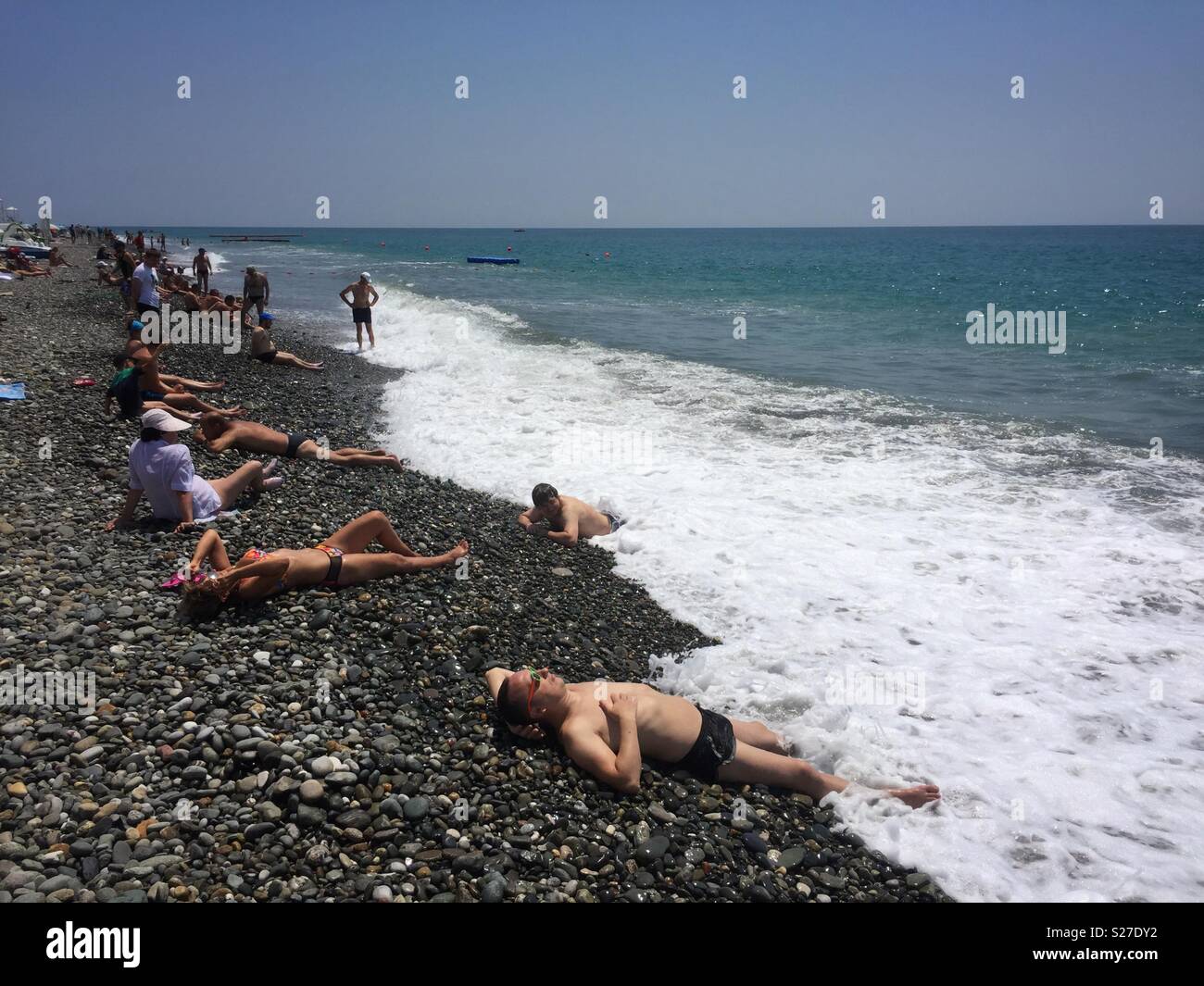 Menschen Sonnen, während auf einem steinigen Strand neben dem Schwarzen Meer, die in dem Verfahren Adler, Sochi in Russland liegen. Stockfoto