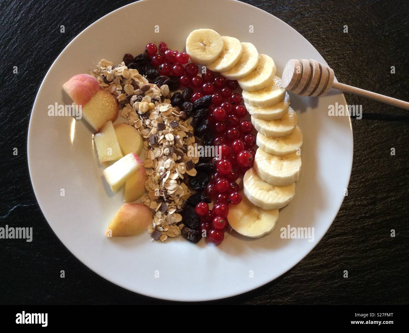 Erhöhten Blick auf Frühstücksflocken und ausgewählte Frucht auf weißen Teller und Löffel Honig aus Holz Stockfoto