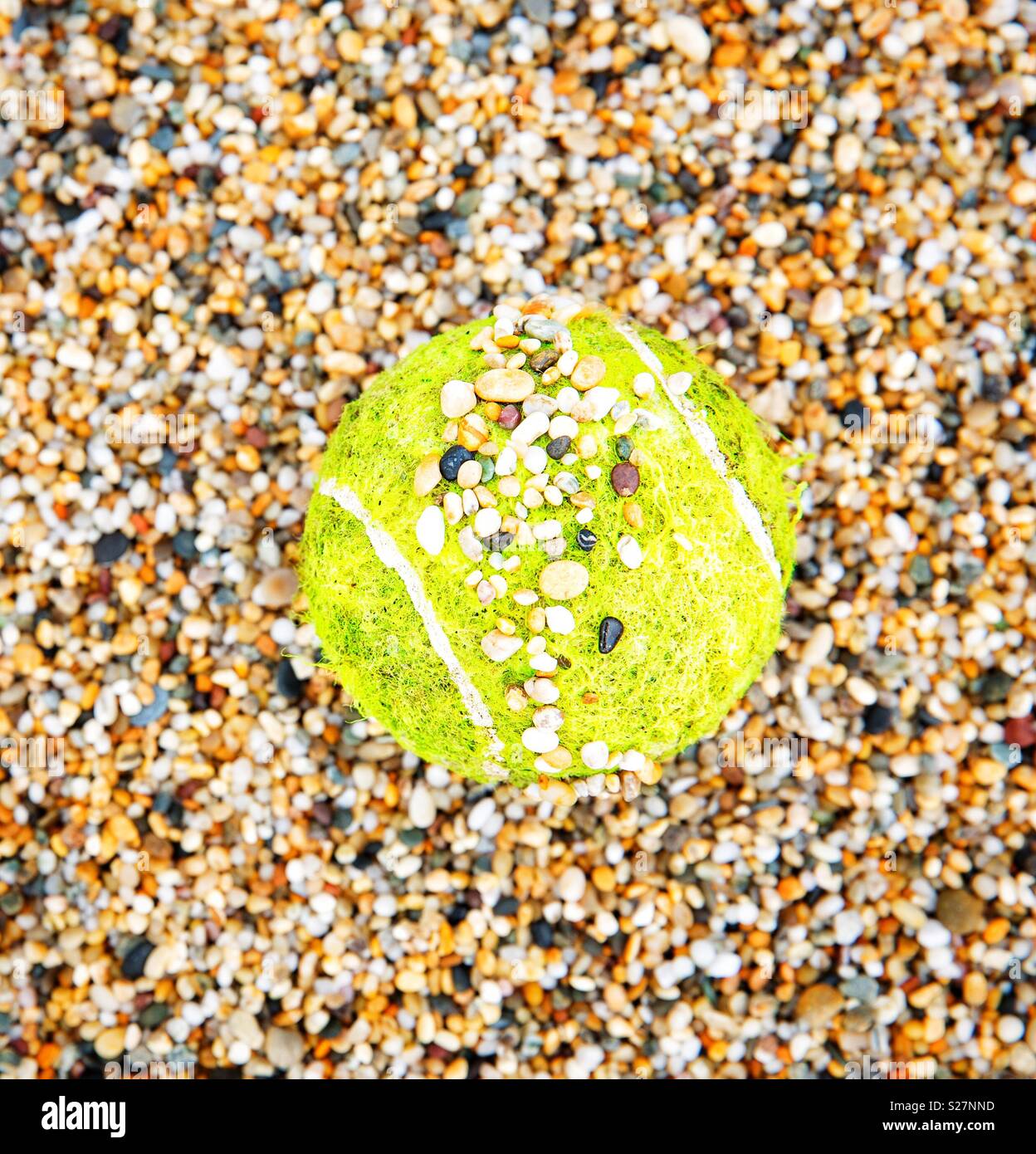 Ein gelber Tennisball auf einem Kies Hof in kleinen Steinchen in einem grass roots Sport Bild abgedeckt Stockfoto