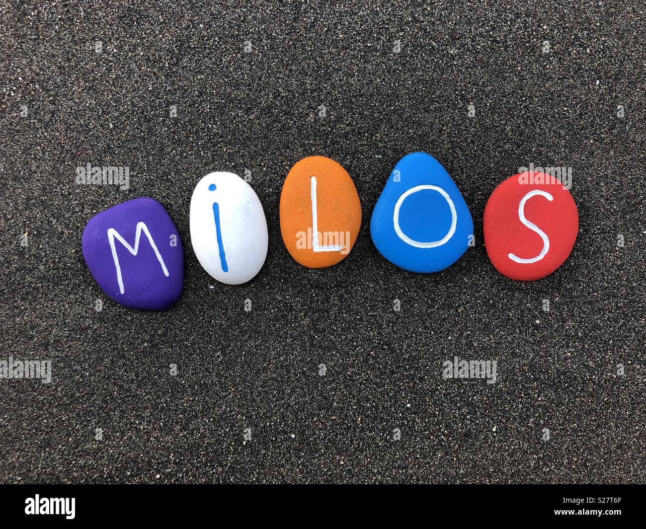 Milos, männliche Vornamen mit mehrfarbig lackiert Stein Briefe über schwarzen vulkanischen Sand Stockfoto