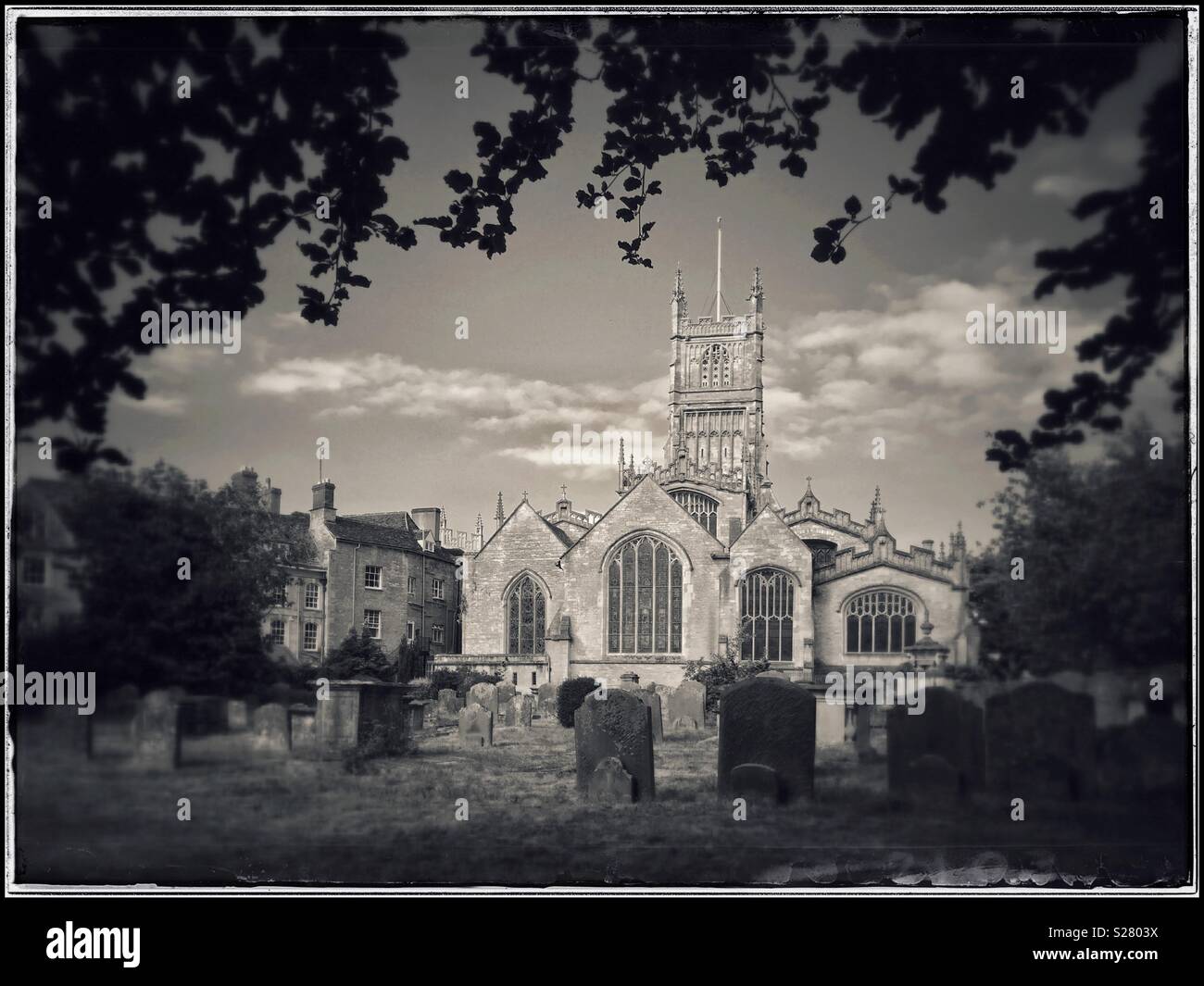 Ein Blick auf die Kirche und Friedhof der St. Johannes Baptist Kirche in Cirencester Gloucestershire, England. Die Kirchen sind durch Blätter und Grabsteine eingerahmt. Foto - © COLIN HOSKINS. Stockfoto