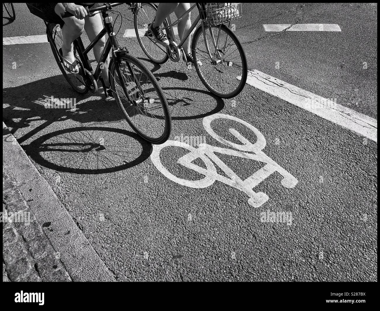 Zwei Radfahrer fahren ihre Fahrräder entlang einer dedizierten Radweg in der Mitte von Kopenhagen (København). Es ist in einem hellen Sommertag, so interessant die Schatten. Ein Bild, das Umweltbewusstsein zu illustrieren. - Smartphone-aufgenommenes Stockfoto