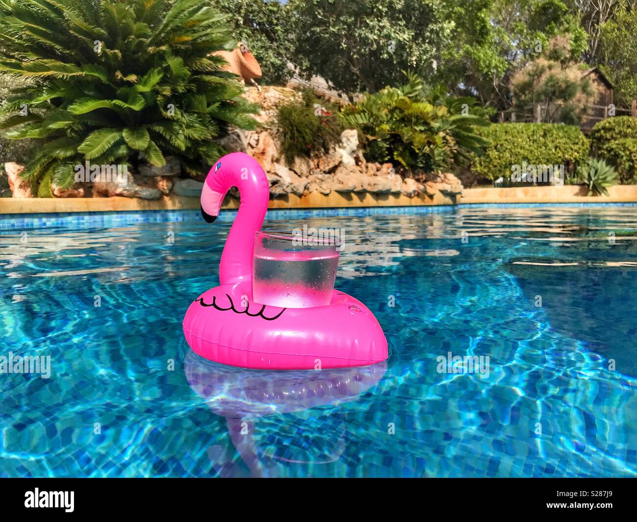 Rosa flamingo Getränke Halter floating in einem Schwimmbad mit einem Glas mit einem eiskalten Getränk. Stockfoto