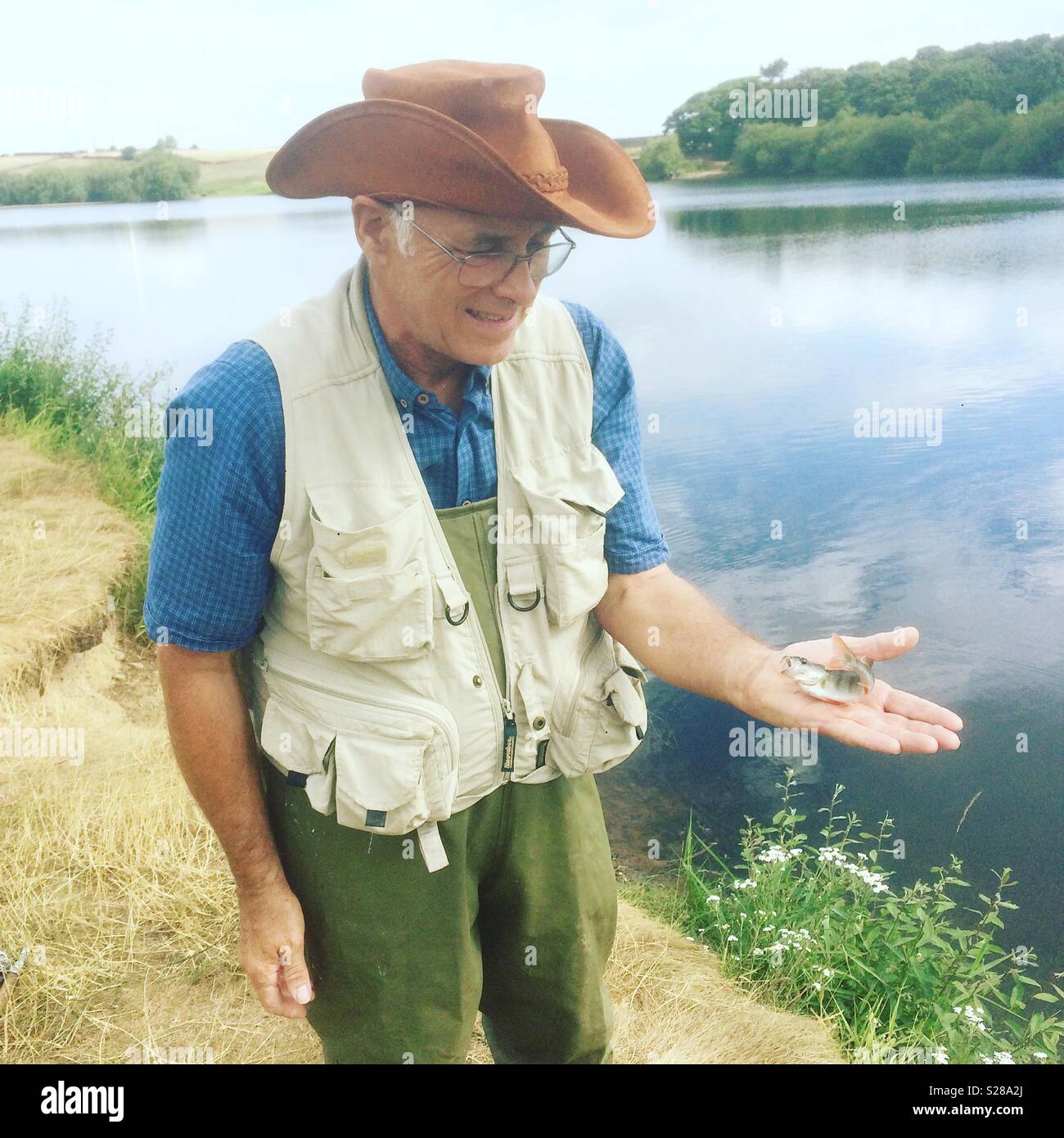 Forelle Fischer mit einem kleinen barsch Fisch, den er bei der Scout Deich Reservoir, Barnsley, South Yorkshire, England, Vereinigtes Königreich. - Smartphone-aufgenommenes Stockfoto