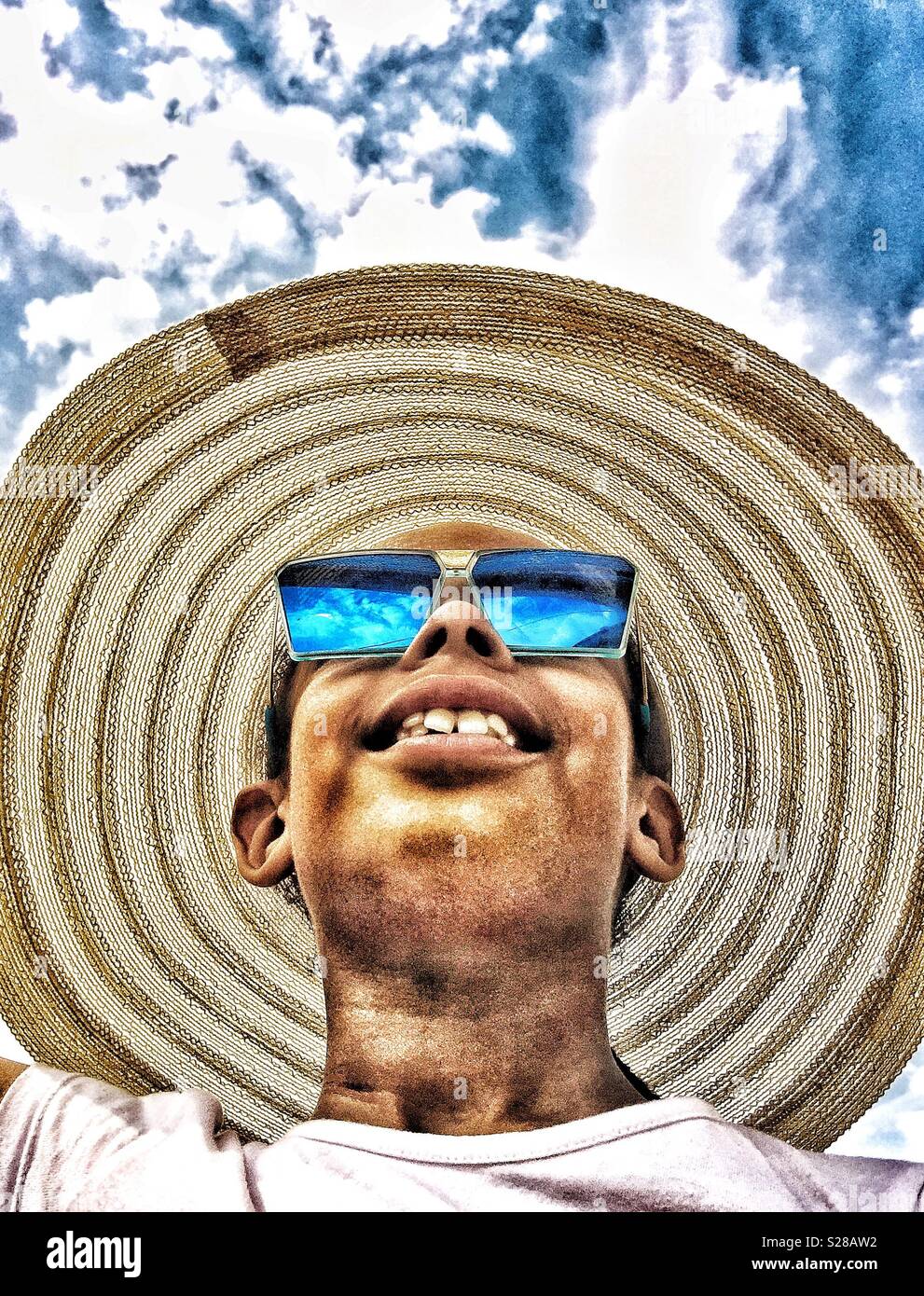 Kind in einem breitrandigen Hut und Sonnenbrille lächelnd - Smartphone-aufgenommenes Stockfoto