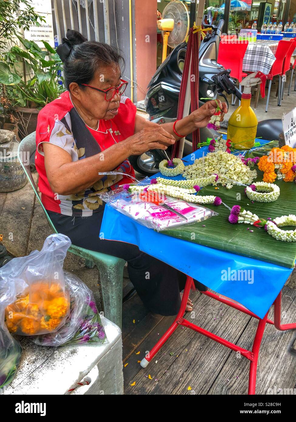 Eine ältere Frau, die Blumendekorationen für eine buddhistische Feier. - Smartphone-aufgenommenes Stockfoto
