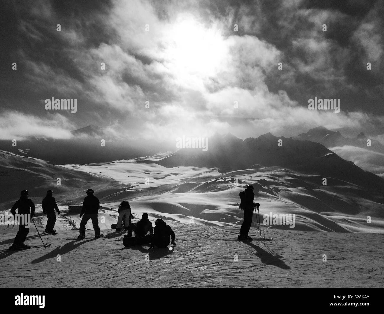 Schwarze und weiße Silhouette der Skifahrer und Boarder auf dem Berg vor der untergehenden Sonne Stockfoto