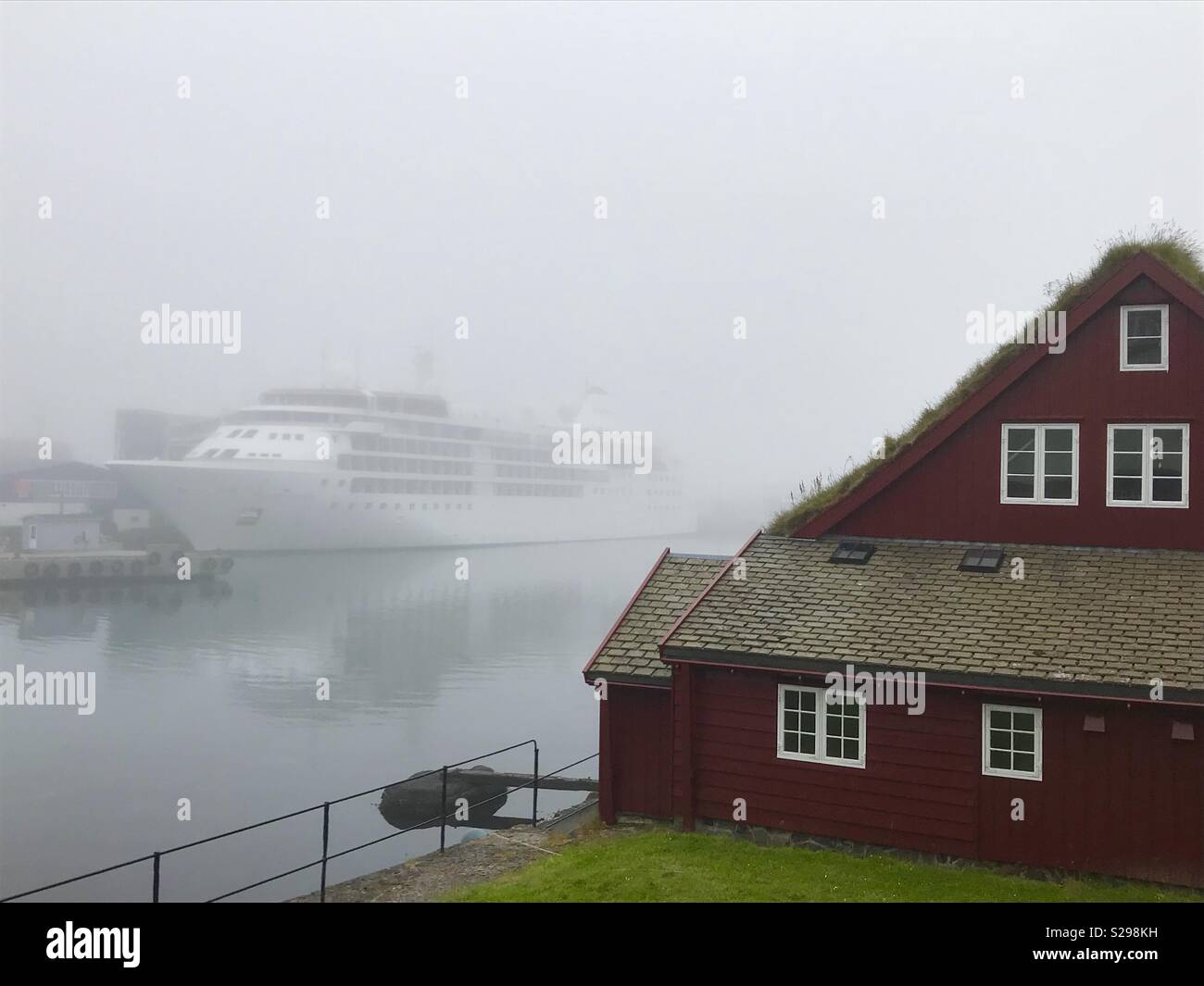 Ein nebeliger Morgen in Halbinsel Tinganes in Tórshavn. Kreuzfahrtschiff im Hintergrund. Stockfoto