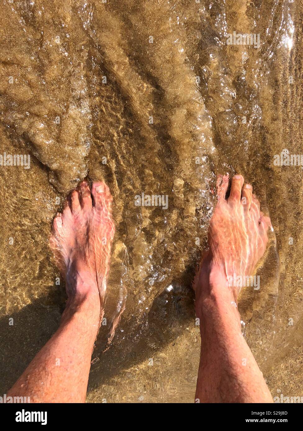 Man's Füßen im Meer an einem Sandstrand Stockfoto