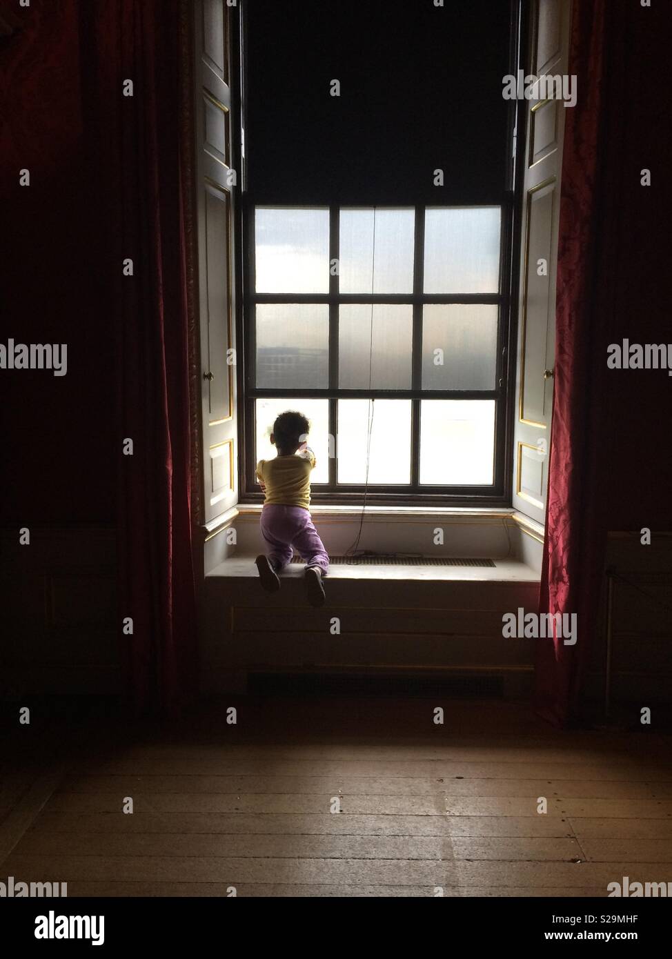Kleines Mädchen durch ein großes Fenster Stockfoto
