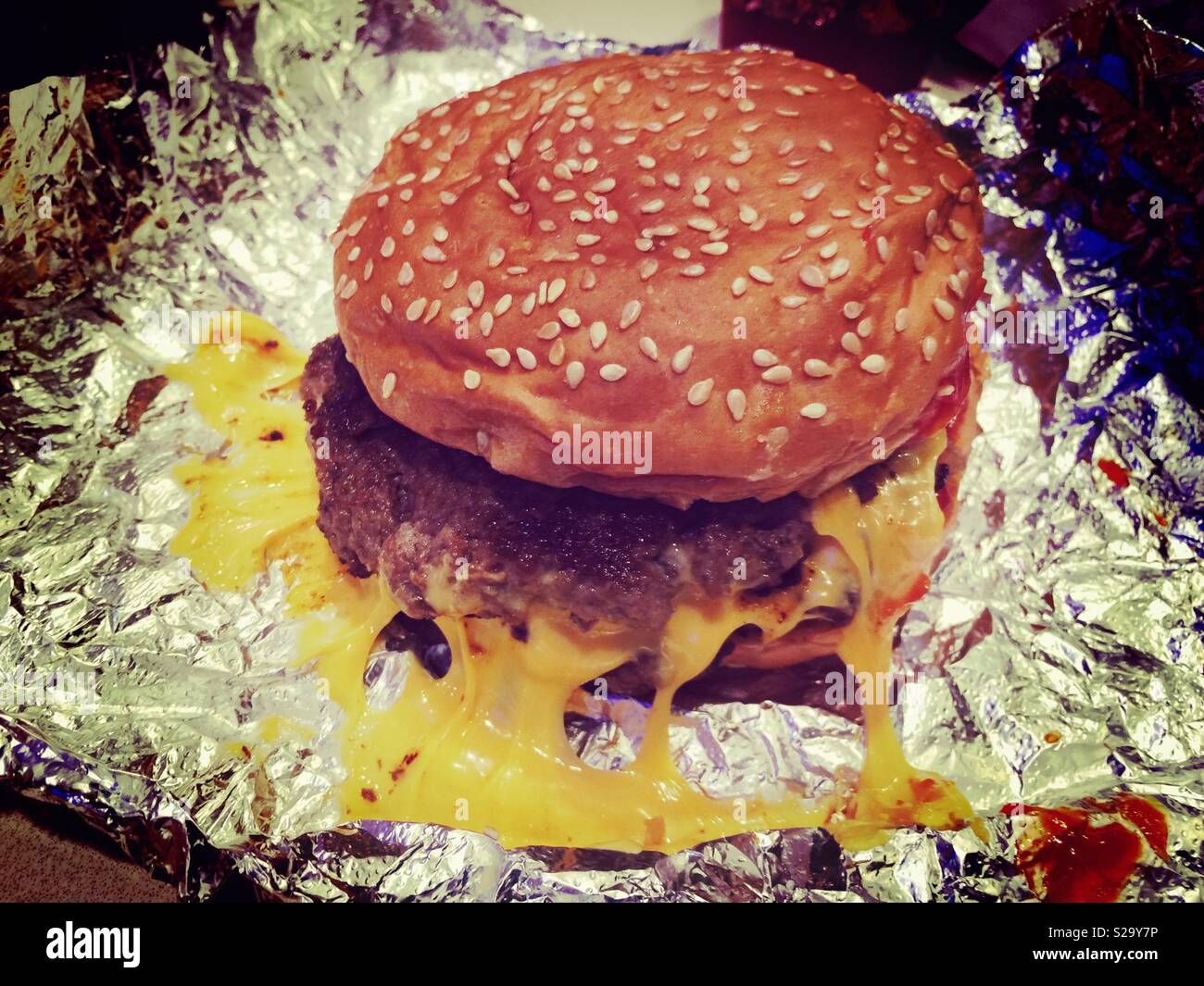 Fettiger Cheeseburger auf Silberfolie Stockfoto
