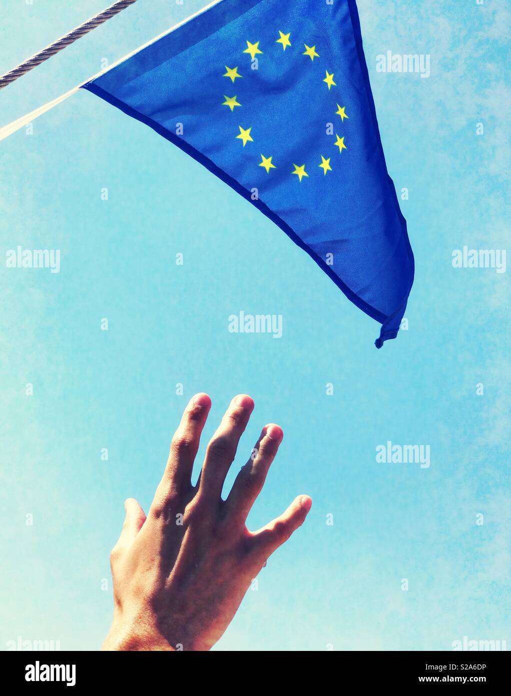 Eine Hand greift nach der EU-Flagge in ein fleckiges blauer Himmel Stockfoto