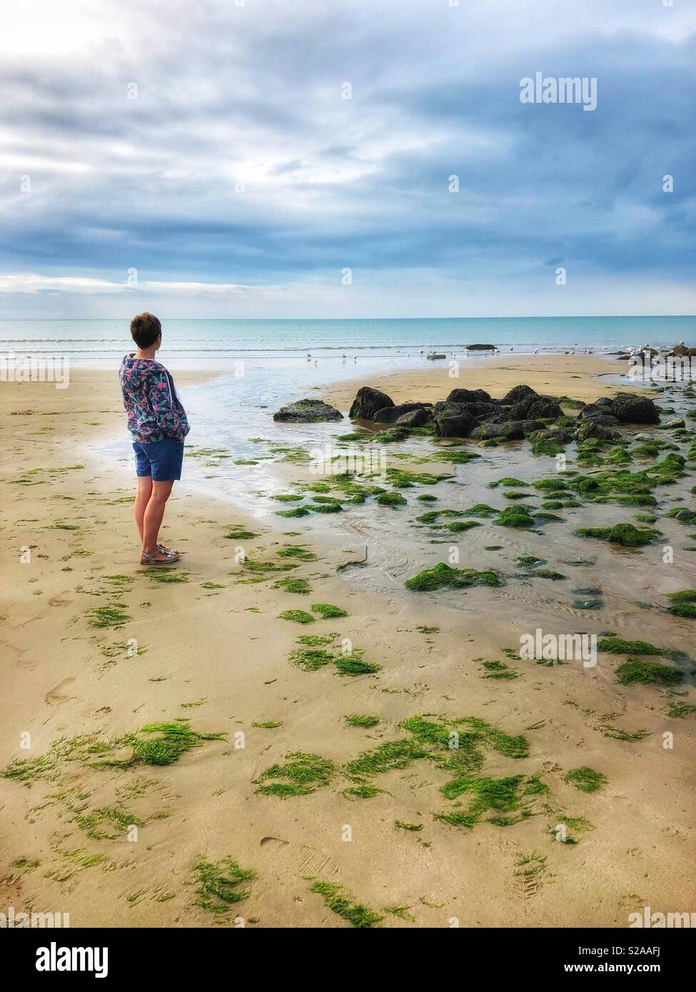 Frau mittleren Alters mit Blick auf den Horizont über den Strand und das Meer. - Smartphone-aufgenommenes Stockfoto