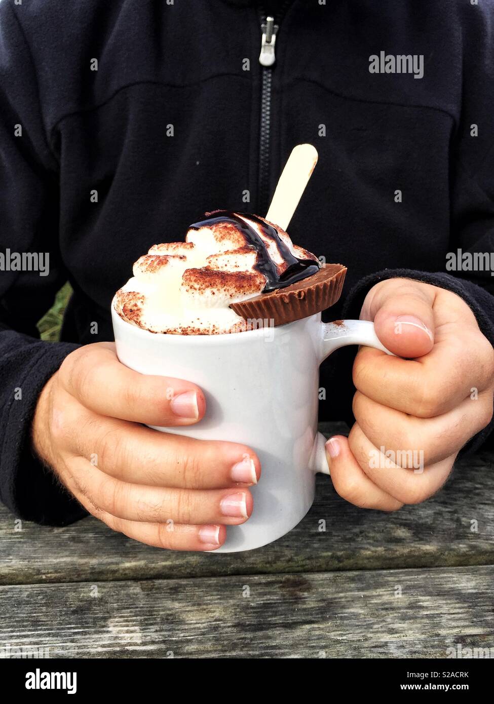 Ein paar menschliche Hände um eine nachsichtige Tasse heiße Schokolade mit Sahne und Schokolade Cookies gewickelt auf Stockfoto