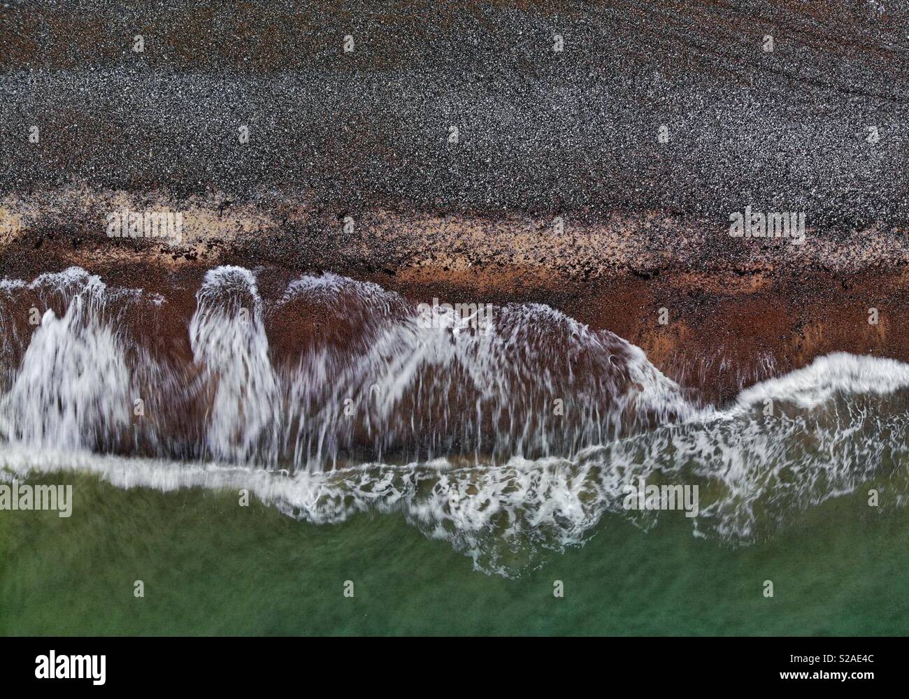 Luftbild der Wellen auf ein Kiesstrand in trüben Abend Licht brechen - Smartphone-aufgenommenes Stockfoto