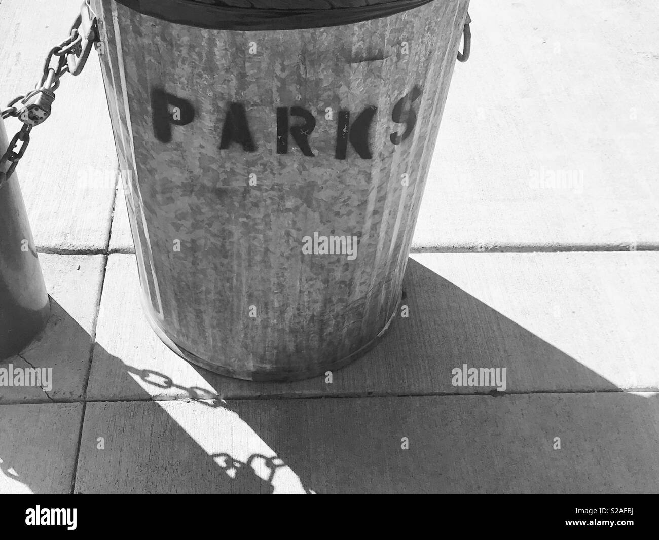Mülleimer im Park - schwarz-weiss Fotografie - Metall Mülleimer Spray auf der Vorderseite gemalt mit dem Wort Parks - Schatten Fotografie Stockfoto