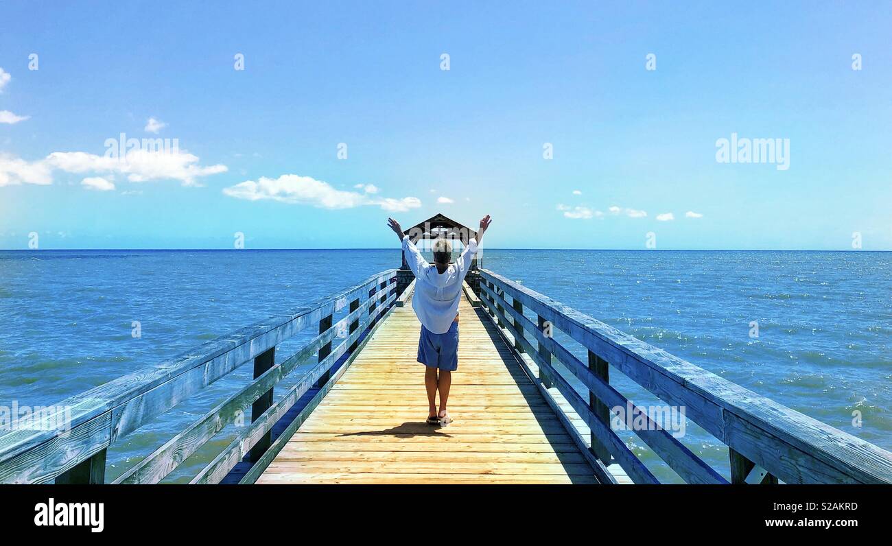 Es gibt die Musik des Lebens. Panoramablick vom Tropical Island Pier mit Freigeistige Anheben der arme junge Mann der schönen türkisblauen Wasser des Pazifischen Ozeans zu umfassen - Smartphone-aufgenommenes Stockfoto