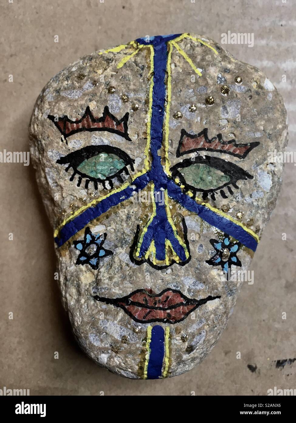 Tribal Art gemalt Rock. Eine bunte Gesicht mit blauen und gelben Linien. - Smartphone-aufgenommenes Stockfoto