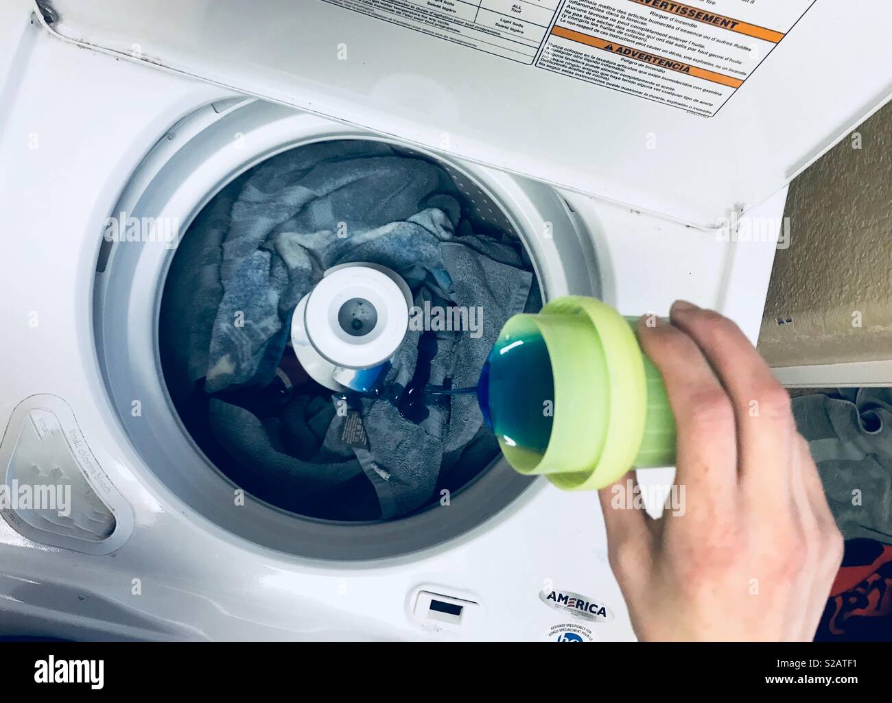 Eine Mamma Gießen Waschmittel in die Waschmaschine voll mit dreckigen Handtücher. Blau Waschmittel, Hausarbeit, Wäsche waschen, Wäsche, Reinigung Stockfoto