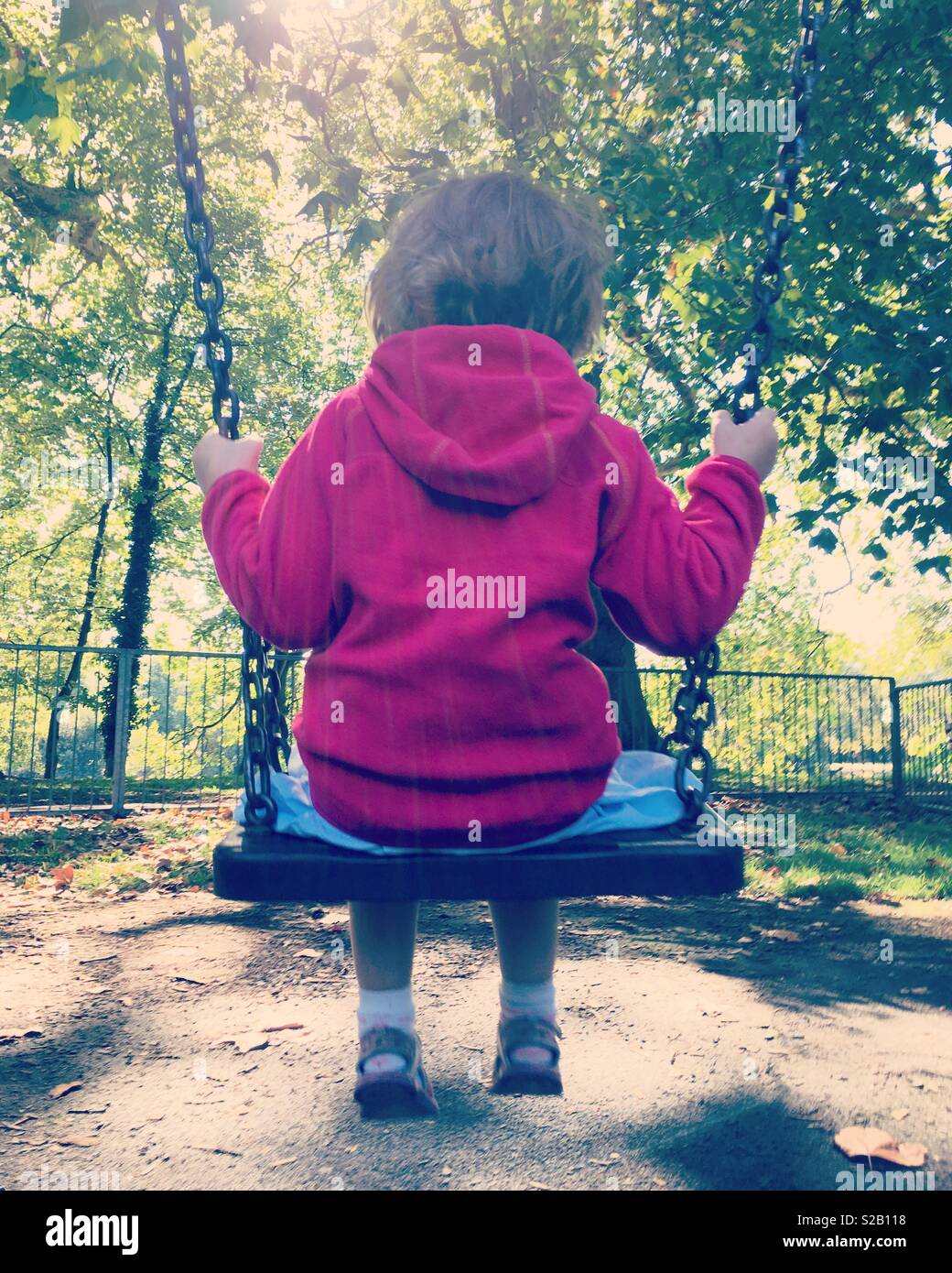 Retro Instagram Foto von einem kleinen Mädchen Alter 4 Jahre / im Alter von vier Jahre alten Schwingen auf dem Schwingen, Schaukeln Park mit Bäumen und Blättern. Großbritannien Stockfoto