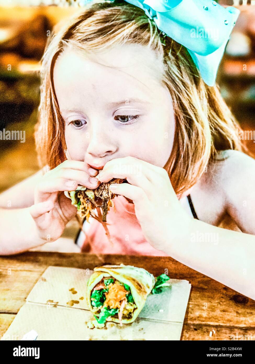 Junge 7 Jahre altes Mädchen mit einem gezogenen Schweinefleisch wrap in einem Restaurant Stockfoto
