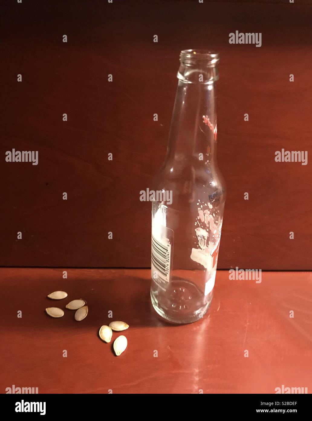 Eine klare leere Soda Pop Flasche sitzt auf einem dunklen Holztisch oben von Kürbis Samen umgeben Stockfoto