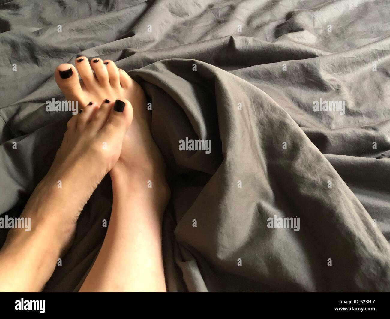Weibliche Füße auf Rumpled Bettwäsche Stockfoto