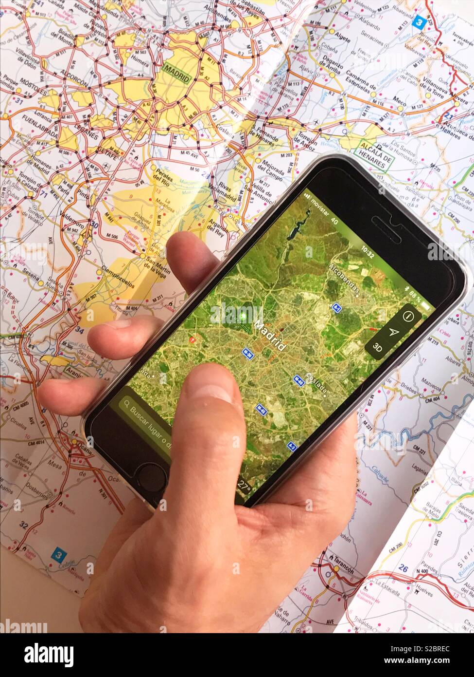 Halten Sie ein Smartphone in der Hand, das eine Karte im Kontrast zu einer Straßenkarte zeigt. - Smartphone-aufgenommenes Stockfoto