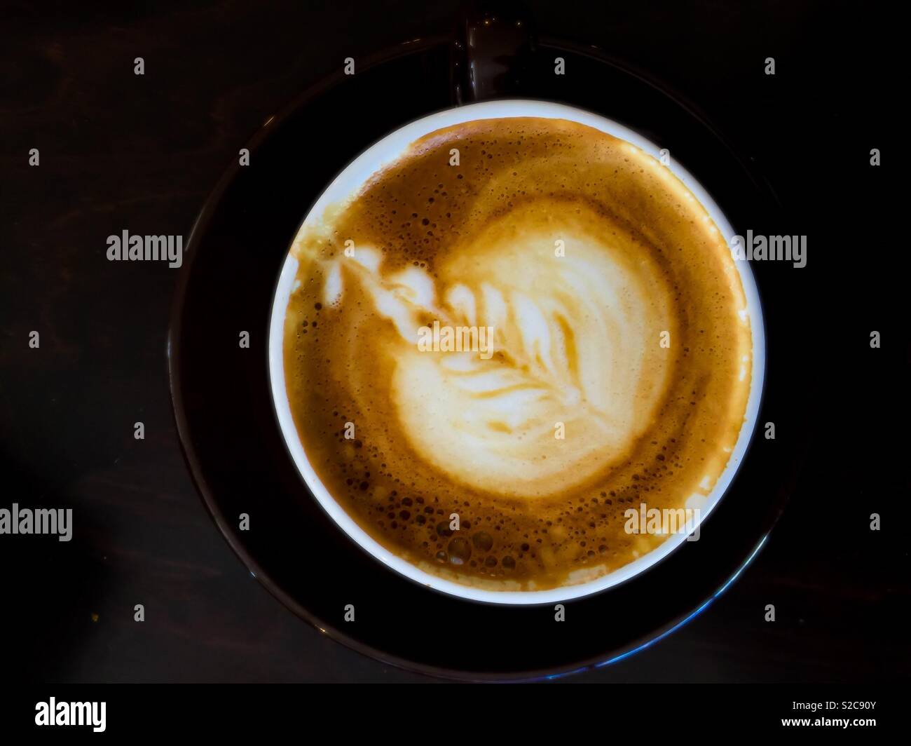 Cappuccino-Design, eine Blume mit dezenter Farbgebung und Schaumstoff treiben auf der Oberfläche einer Kaffeetasse. Vergänglich. Tastbetätigung. Verdaulich. - Smartphone-aufgenommenes Stockfoto