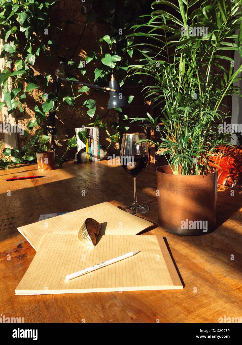 Autoren Schreibtisch mit warmer Beleuchtung im Loft Stil mit Pflanzen und Notebooks und Glas Rotwein Stockfoto