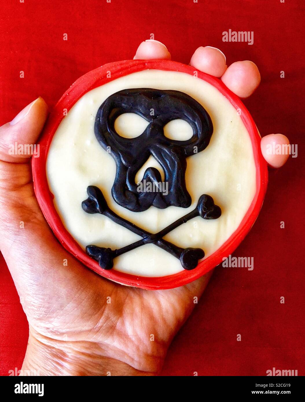 Gift schwarz Schädel Cookie in der Hand der Person auf rotem Hintergrund - Smartphone-aufgenommenes Stockfoto