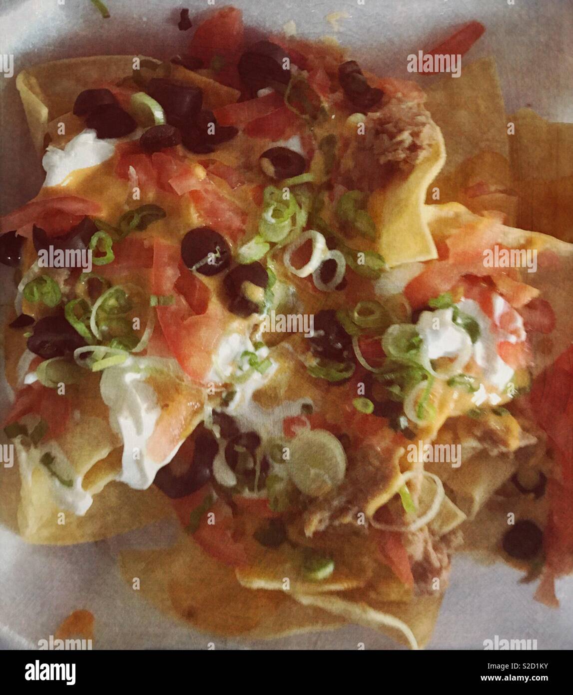 Eine Platte oder Nachos mit extra Toppings. Sauerrahm, Schnittlauch, Zwiebeln, Oliven, Paprika, Tomaten und Käse Stockfoto