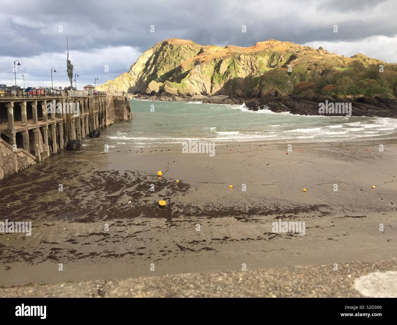 Ilfraconbe Hafen mit Strand Meer und sonnige Klippen gegen einen dunklen und stürmischen Himmel Stockfoto