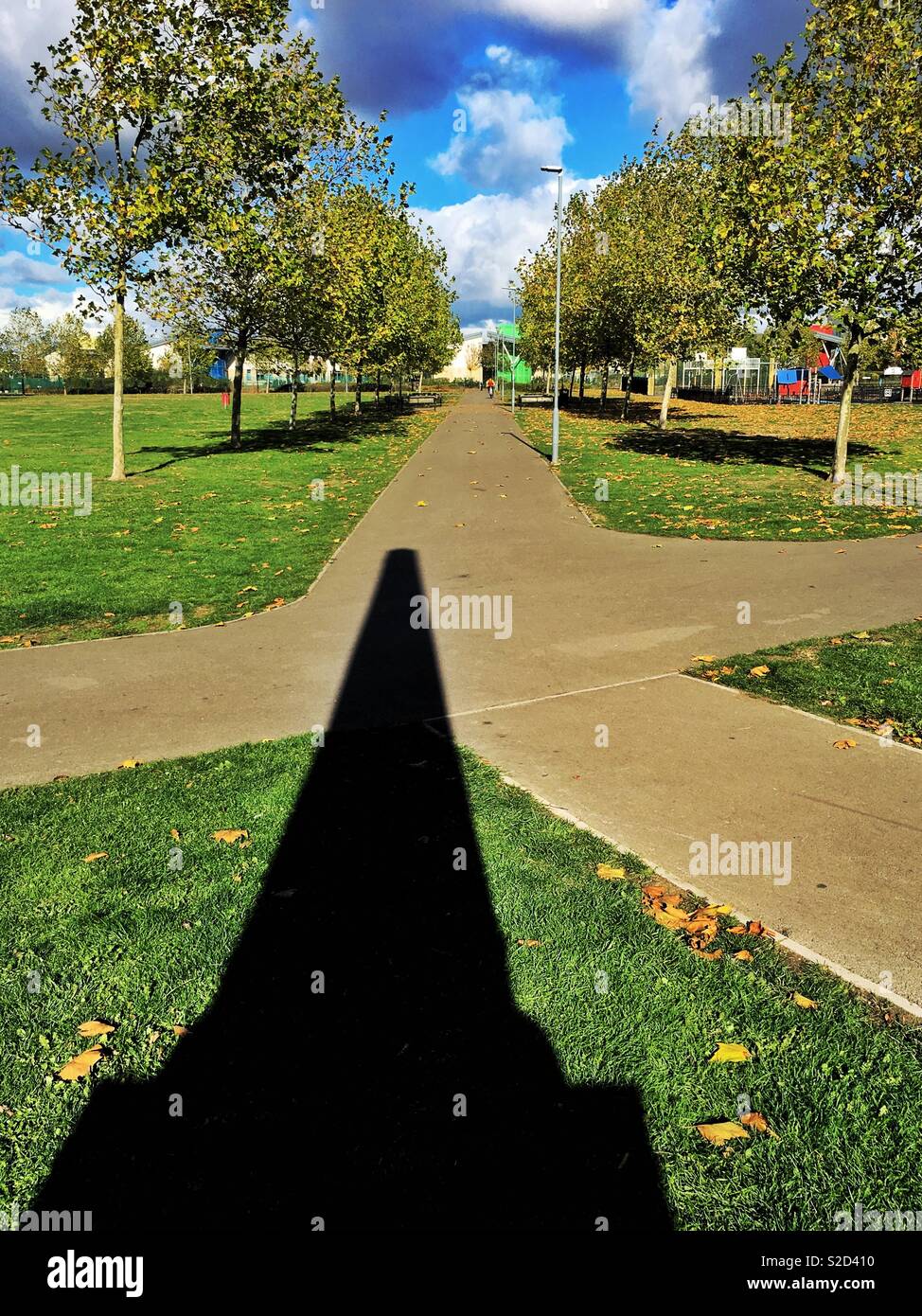 Lange Schatten der ein Monument auf einem Weg Kreuzung in einem von Bäumen gesäumten Park Stockfoto