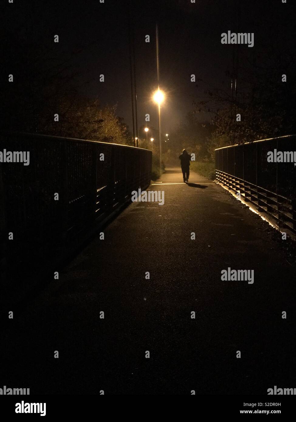 Mann entfernt, in Richtung einer Straßenlaterne, über eine Brücke bei Nacht Stockfoto