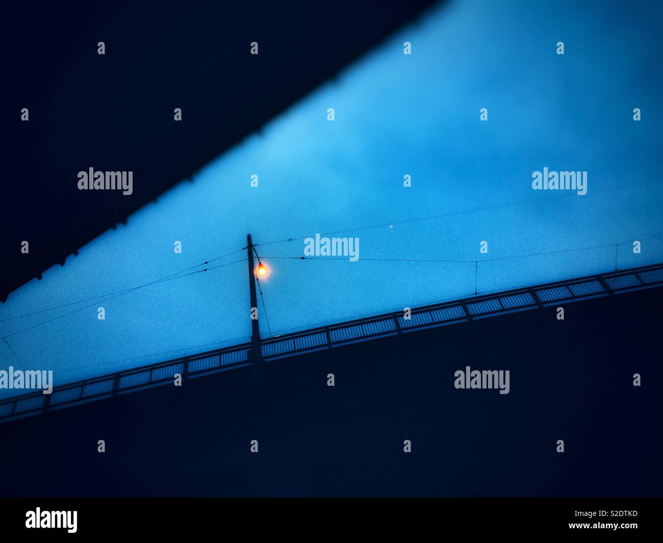 Single beleuchtete Straßenlaterne in der Dämmerung vor blauem Himmel in einer Grafik abstrakter Film Noir Stil. Stockfoto