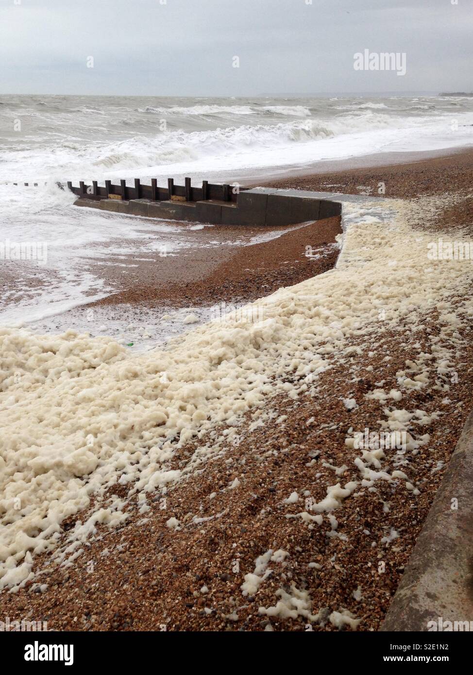 Schaumstoff vom Meer auf einem Kiesstrand an einem stürmischen Tag durchgebrannt - Smartphone-aufgenommenes Stockfoto