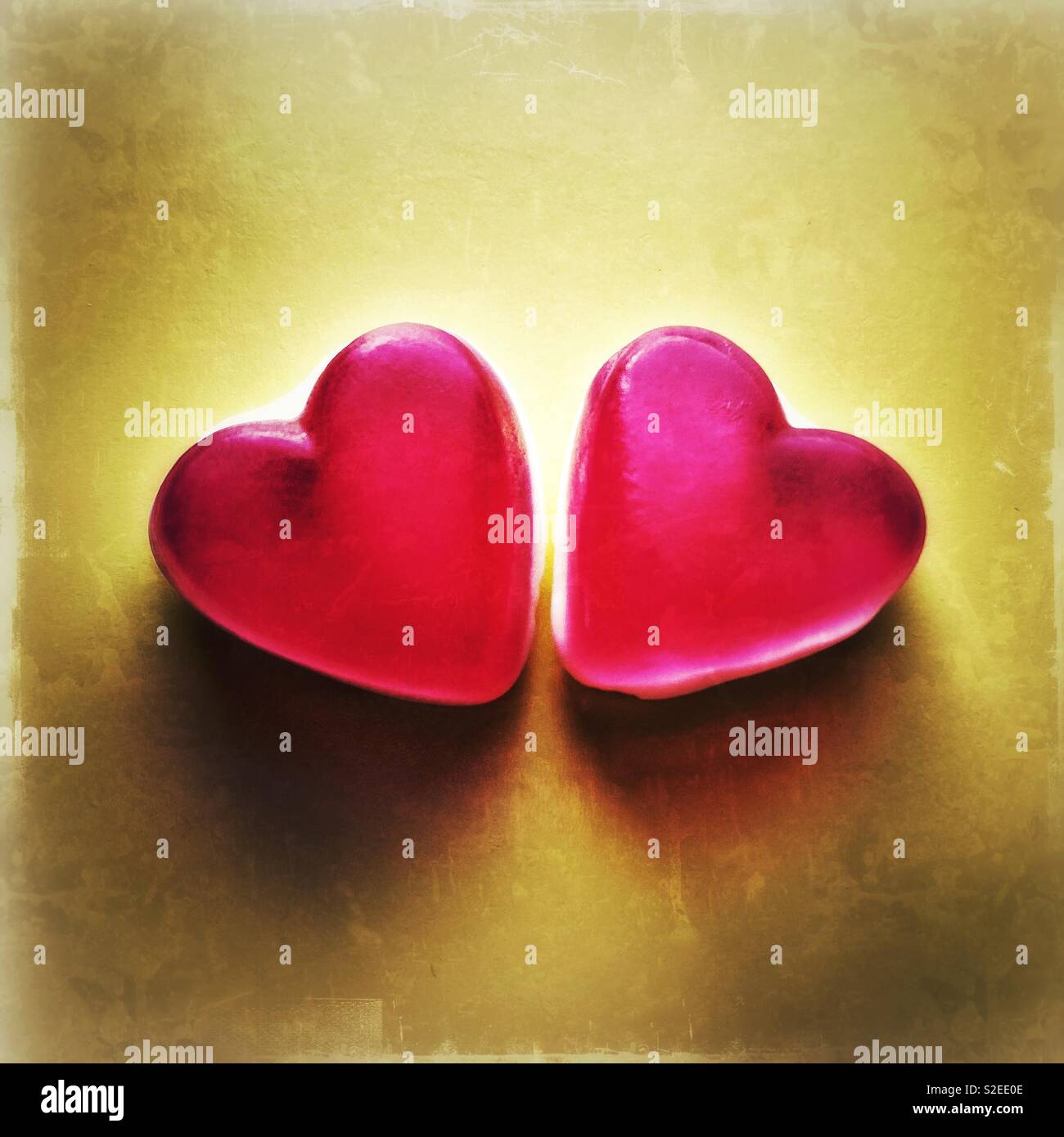 Zwei rote Haribo-herzförmige Gelee-Süßigkeiten nebeneinander mit gelbem Hintergrund, Schatten sorgen für Atmosphäre. - Smartphone-aufgenommenes Stockfoto