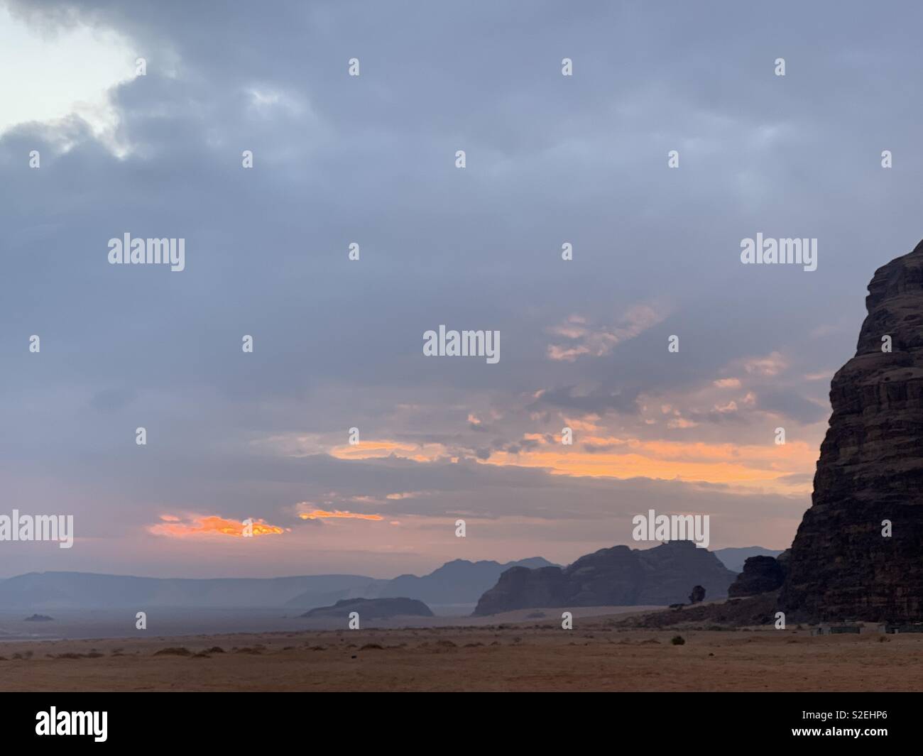 Sonnenaufgang über Wadi Rum an einem bewölkten Morgen. Lichtschimmer knallen durch. Stockfoto