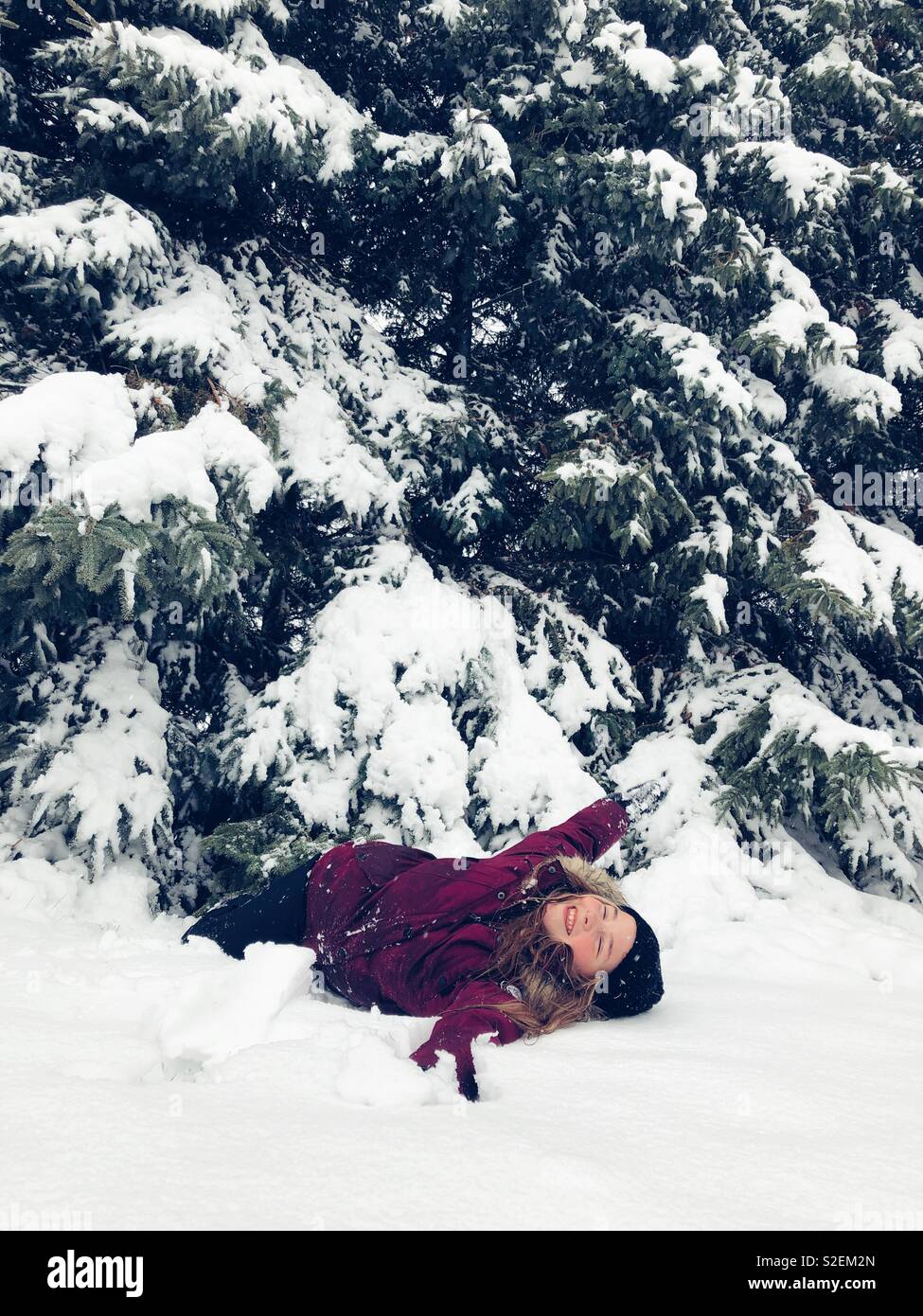 Tween Mädchen spielen im Schnee unter hohen Evergreens Stockfoto