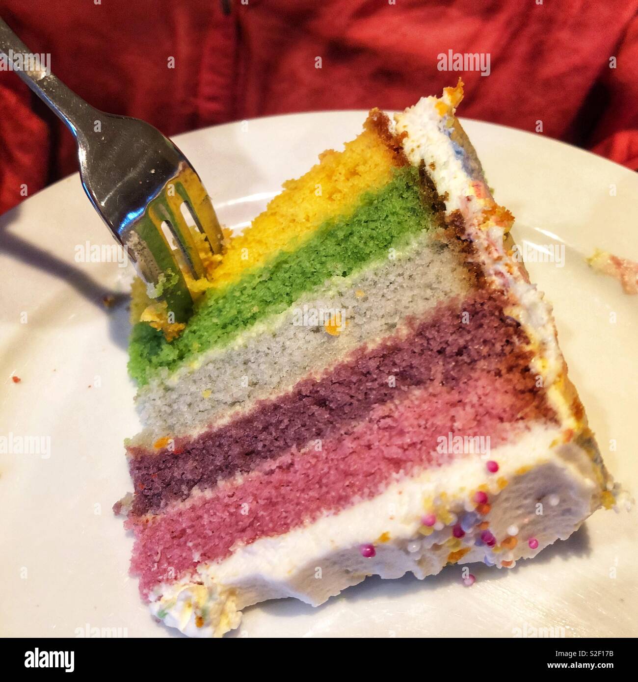 Person essen ein Stück der bunten, rainbow Kuchen mit einer Gabel Stockfoto