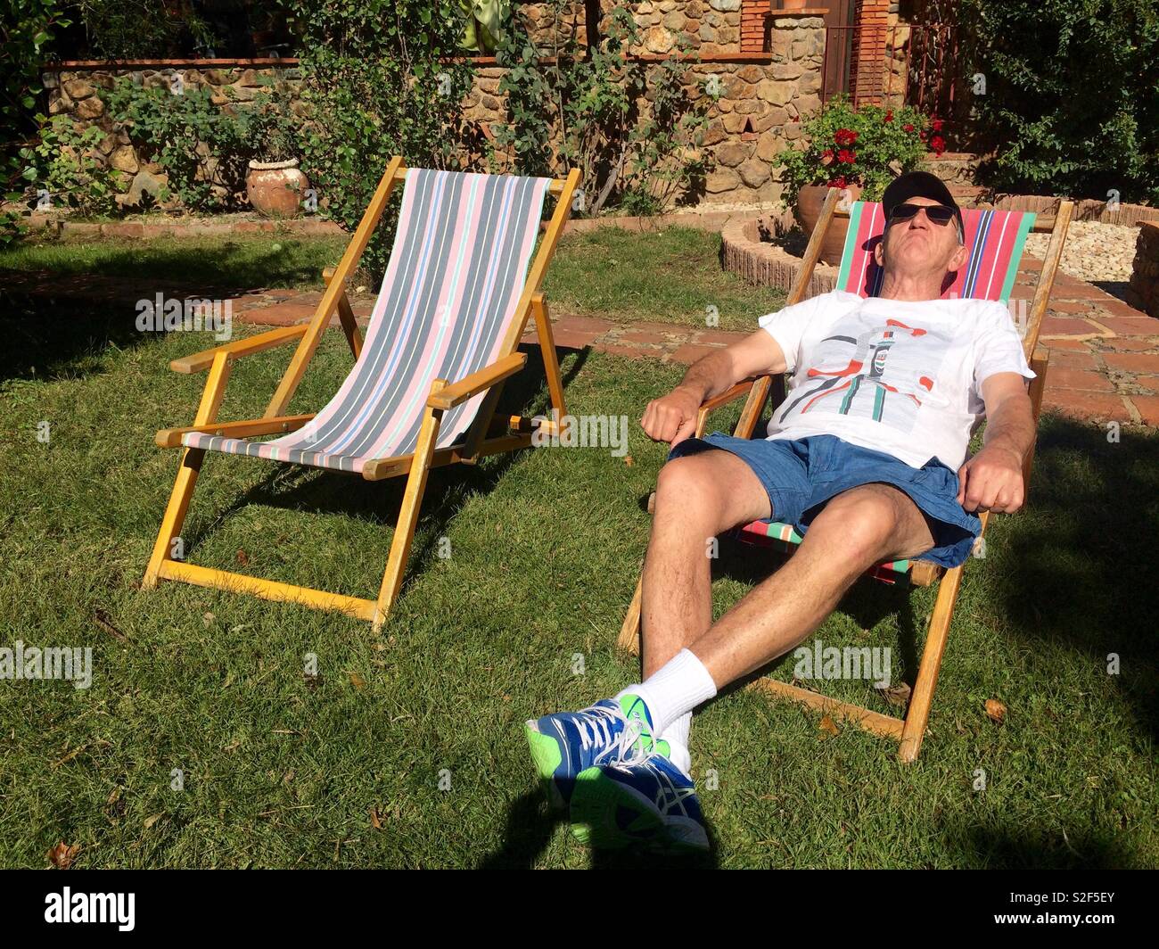 Mann lag auf Deck chair Fang ein Suntan an einem sonnigen Tag in einem Garten Stockfoto