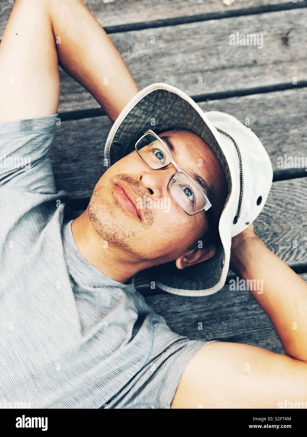 Im mittleren Alter asiatischer Mann mit Wanne Hut und Brille suchen Festlegung auf Camping Plattform in der kanadischen Wildnis Stockfoto