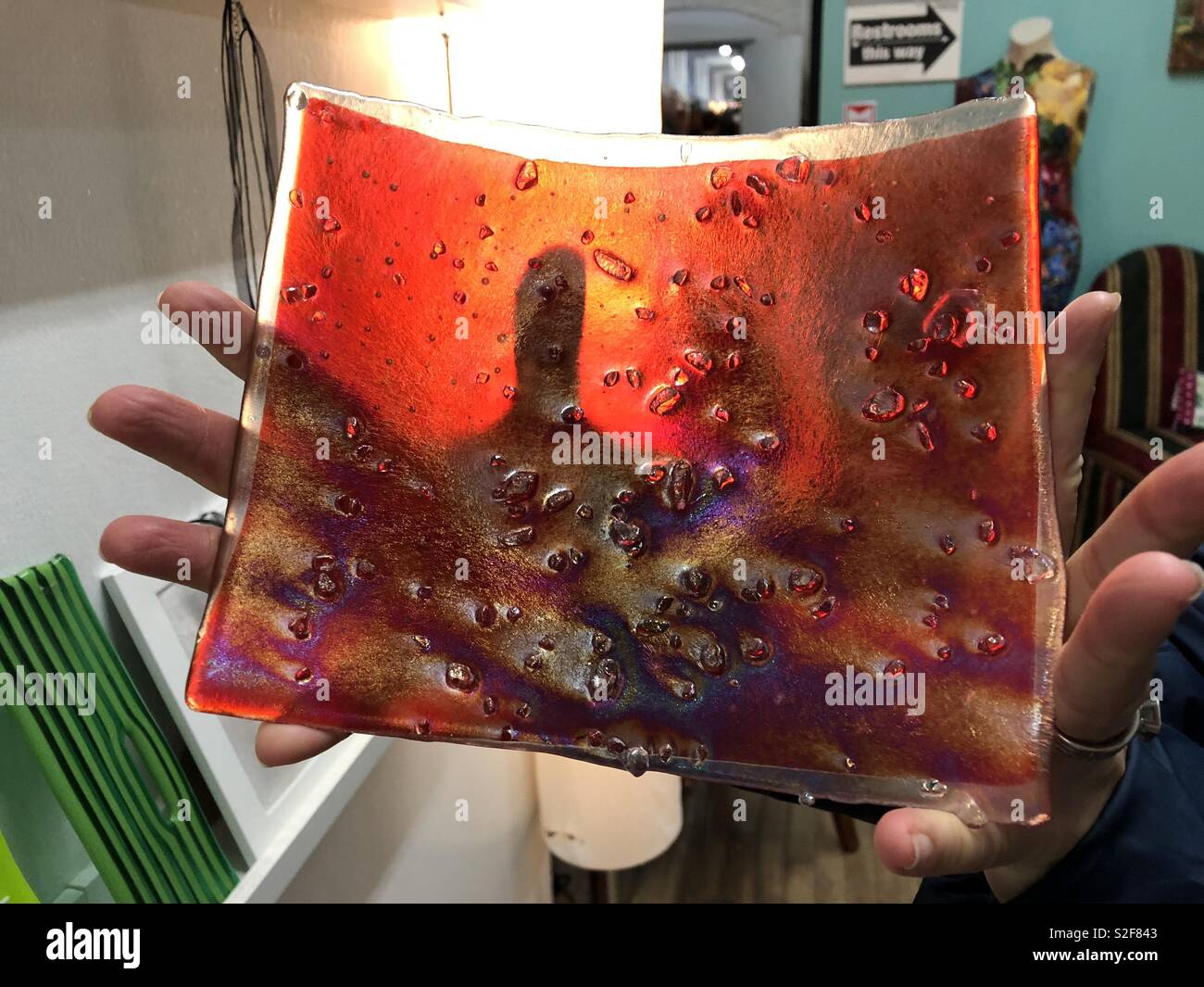 Irisierend rot Glas handgefertigte Servierplatte in Händen an Artist's Studio statt - Smartphone-aufgenommenes Stockfoto