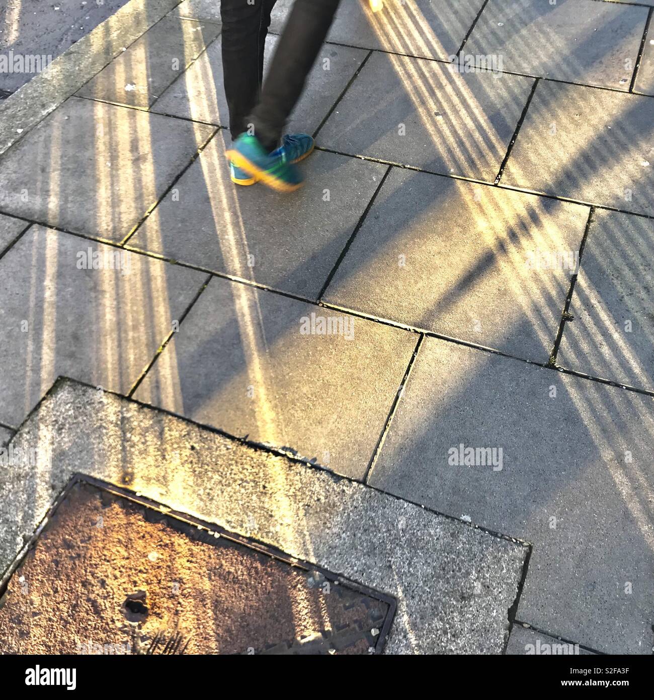 Eine Person geht durch geometrische Schatten auf einem Bürgersteig - Smartphone-aufgenommenes Stockfoto